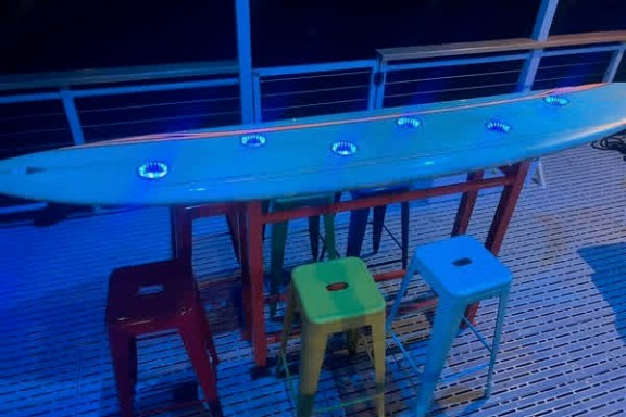 Surfboard table with stools and blue lights on a deck.