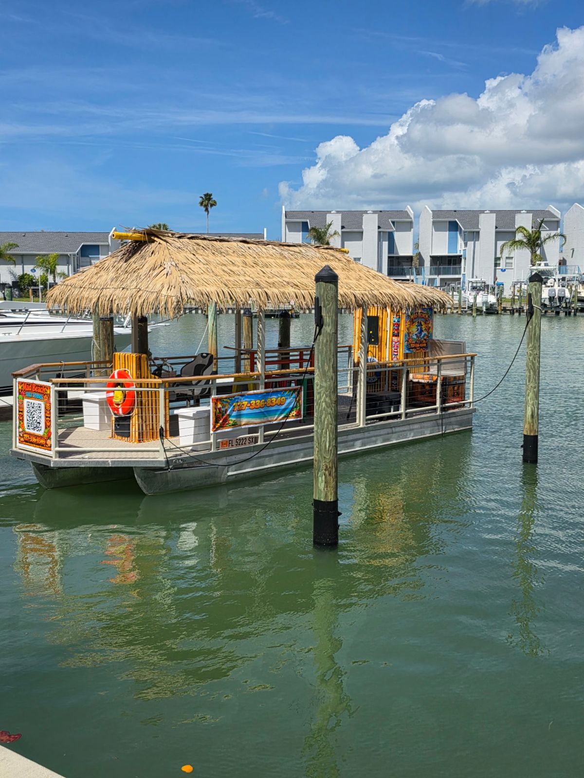 Tiki-style boat docked on calm water with buildings in the background.